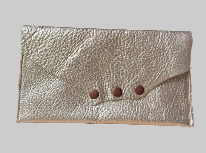 Gold leather clutch with button details on a wooden surface